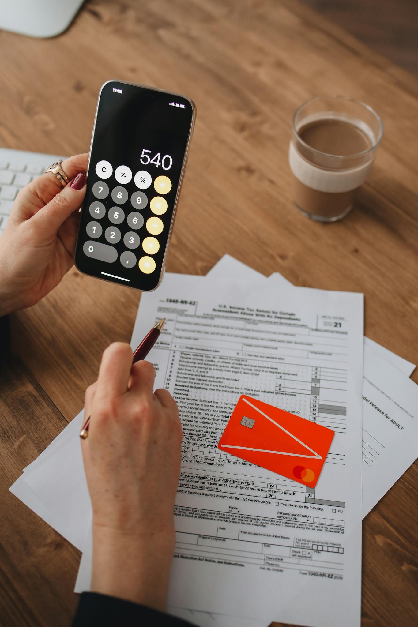 A person uses a smartphone calculator over tax documents on a wooden table.
